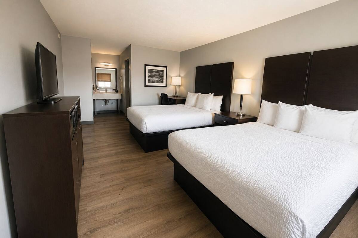 A hotel room with two beds, a TV, a desk, and a bathroom.