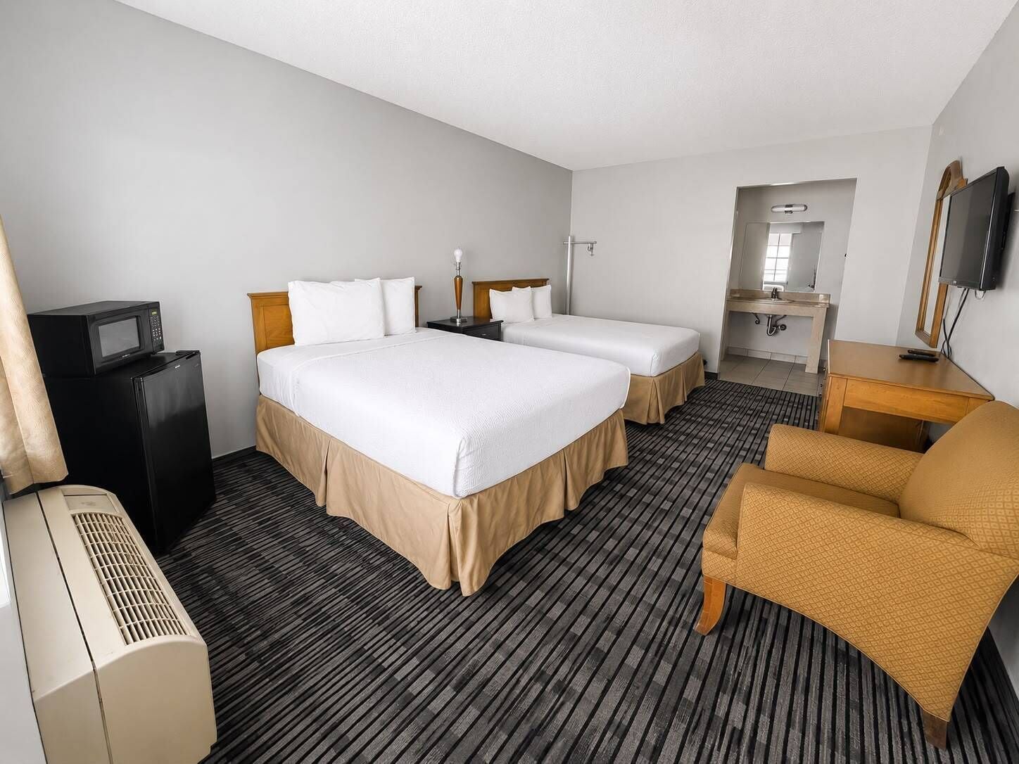 A hotel room with two beds, a desk, a television, and a bathroom.