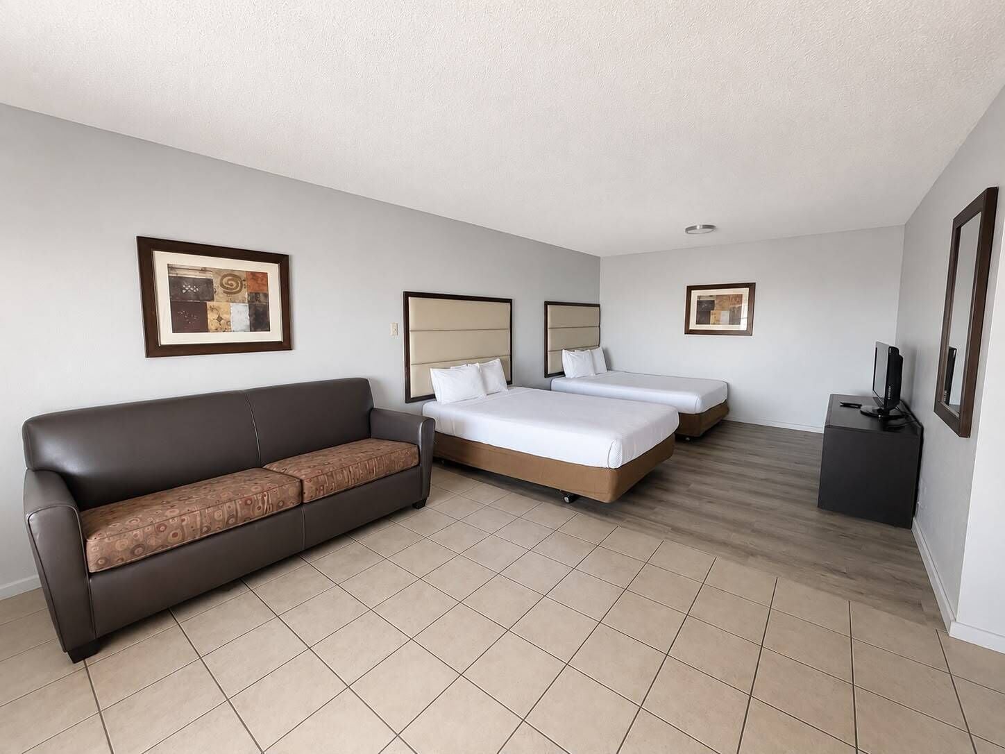 A hotel room with a sofa, two beds, a TV, and artwork on the walls.