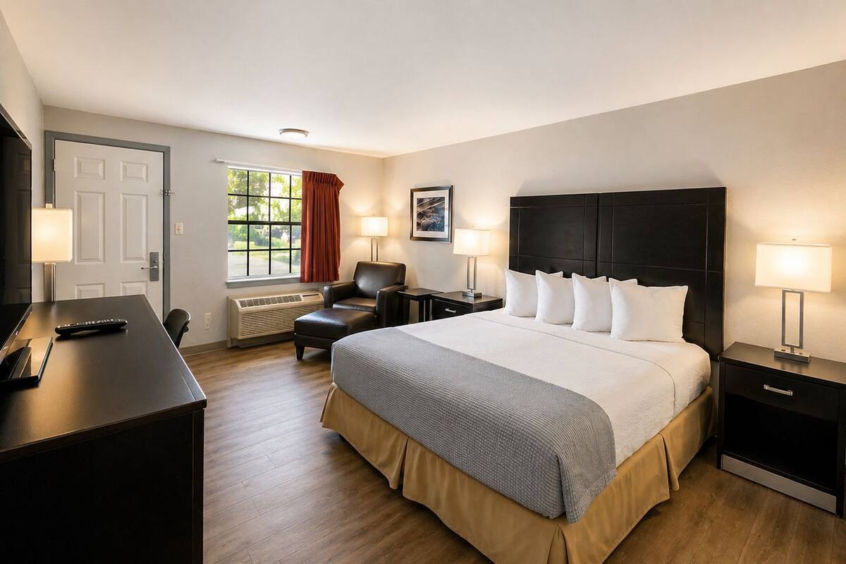 A hotel room with a large bed, a desk, a chair, a window with curtains, and a wall-mounted TV.