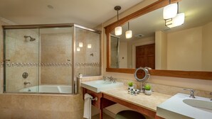 A modern bathroom with a glass-enclosed shower, two sinks, a large mirror, and a vanity with a stool.