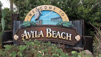 Willkommensschild für Avila Beach mit Küstenlandschaft und einem Seevogel.