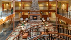A spacious lobby with a central fireplace, multiple seating areas, and a staircase connecting different levels. - Avila Village Inn (Avila Beach)