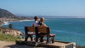 A couple sitting on a bench overlooking a coastal view with a clear sky.
