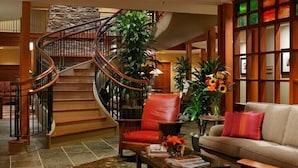 A spacious lobby with a curved staircase, a leather armchair, a sofa, and a coffee table with books and a vase of flowers. - Avila Village Inn (Avila Beach)