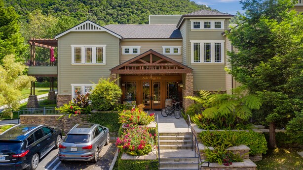 A two-story house with a front porch, a garage, and a driveway with two cars parked.
