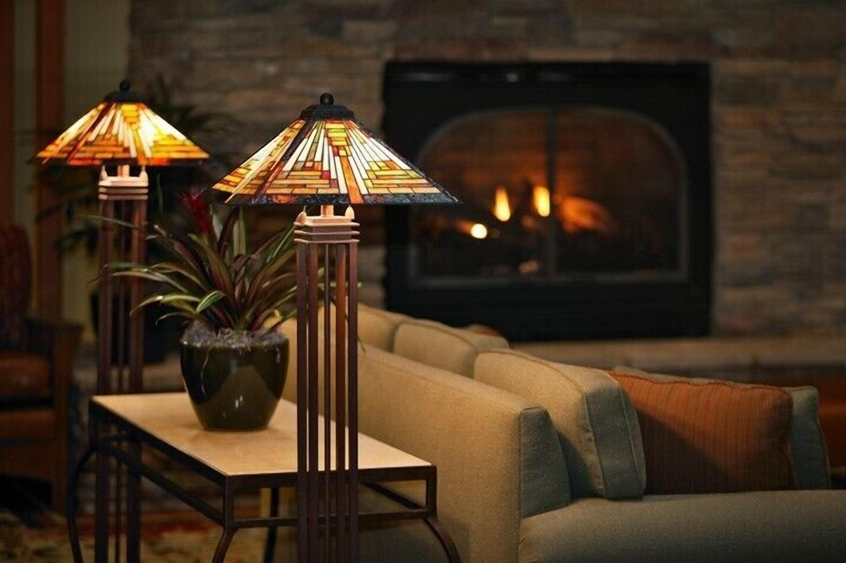 A cozy living room with a fireplace, two floor lamps, and a potted plant.