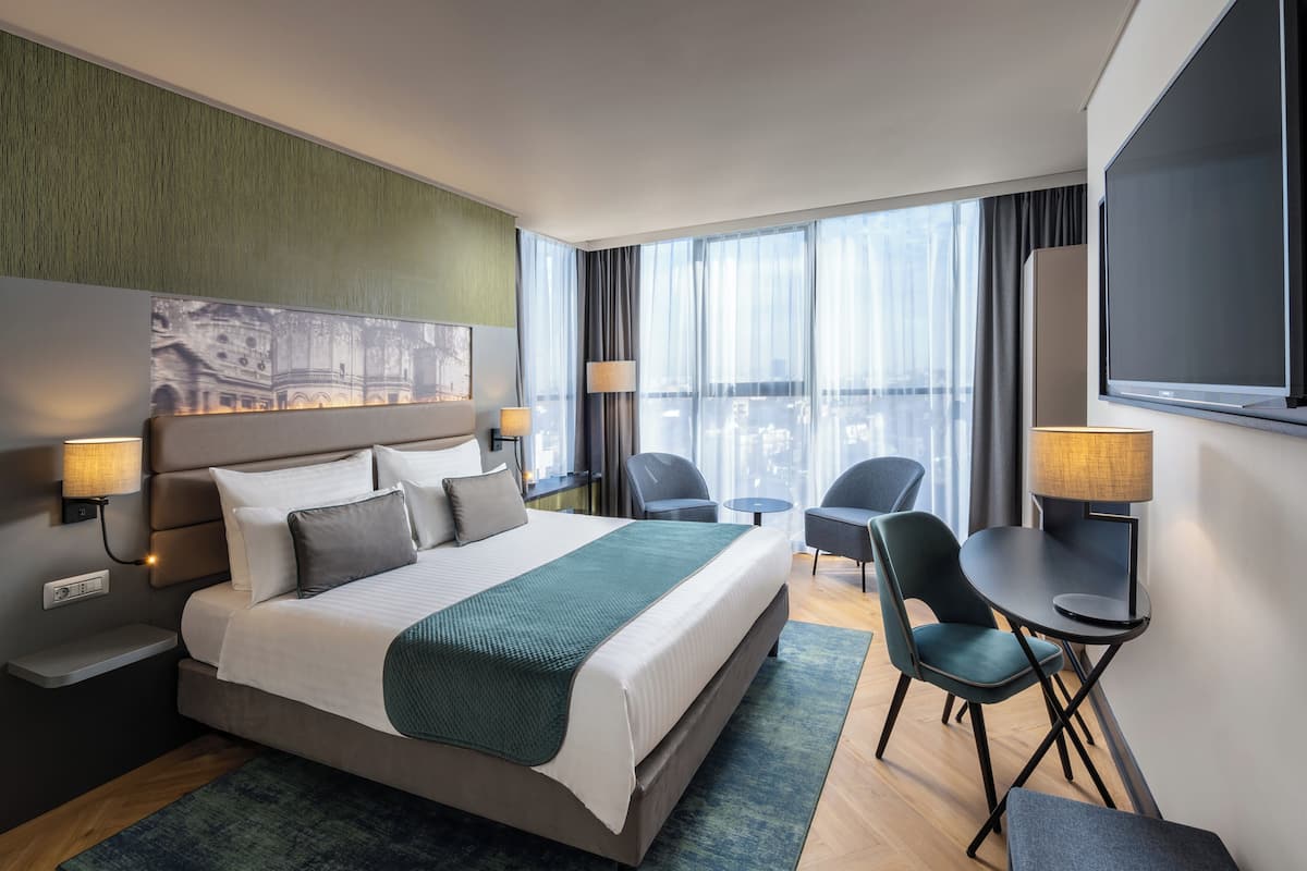 Et moderne hotelværelse med en stor seng, to stole, et lille bord og et fjernsyn.