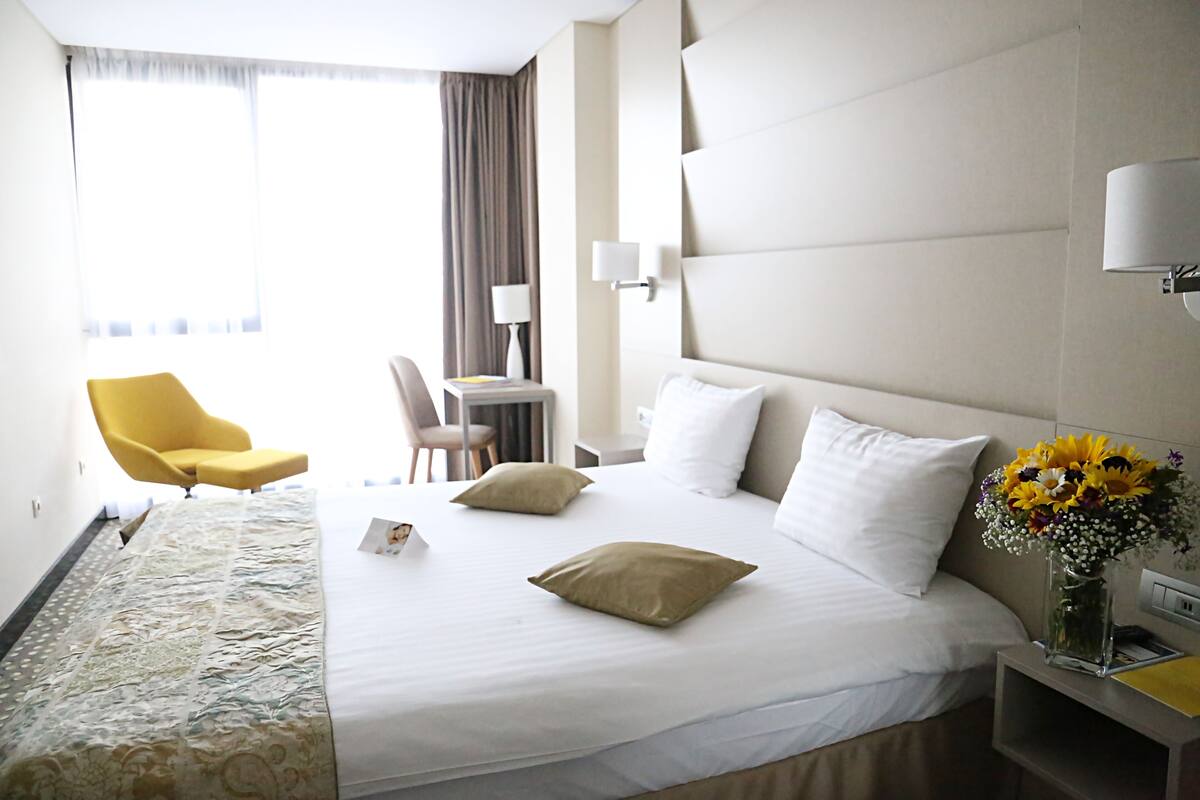 Une chambre d’hôtel avec un lit, un bureau, une chaise et un vase de fleurs.