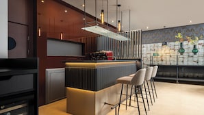 Un área de bar moderna con una barra elegante, taburetes, iluminación colgante y jarrones decorativos.