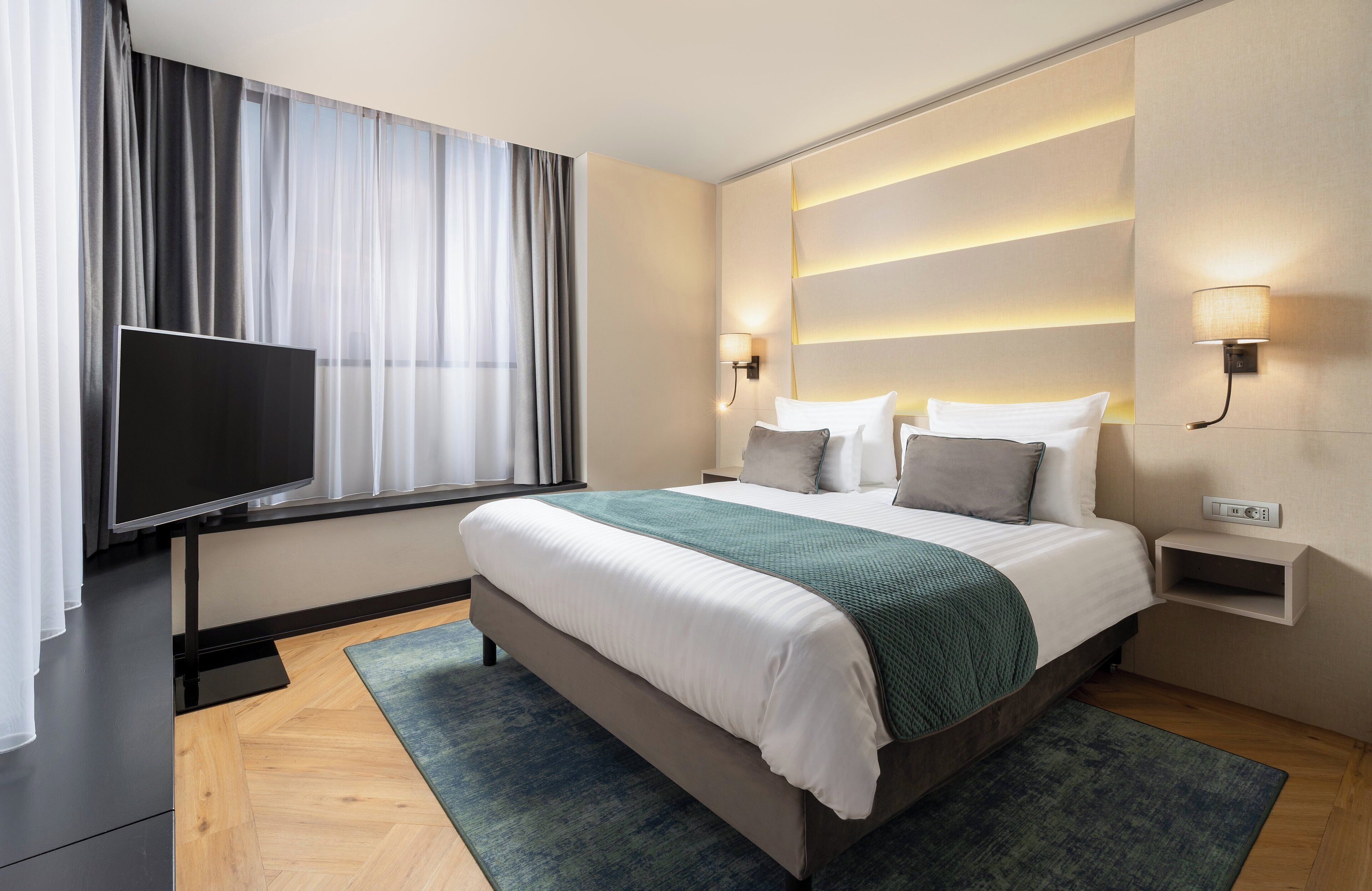Une chambre d’hôtel moderne dotée d’un grand lit, d’une télévision à écran plat et d’une table de chevet avec une lampe.