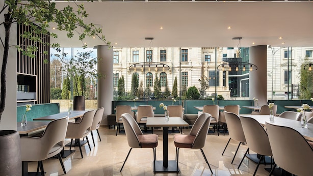 Un restaurante moderno con vistas a un edificio histórico, que ofrece una combinación de mesas dentro y fuera, y un diseño limpio y contemporáneo.