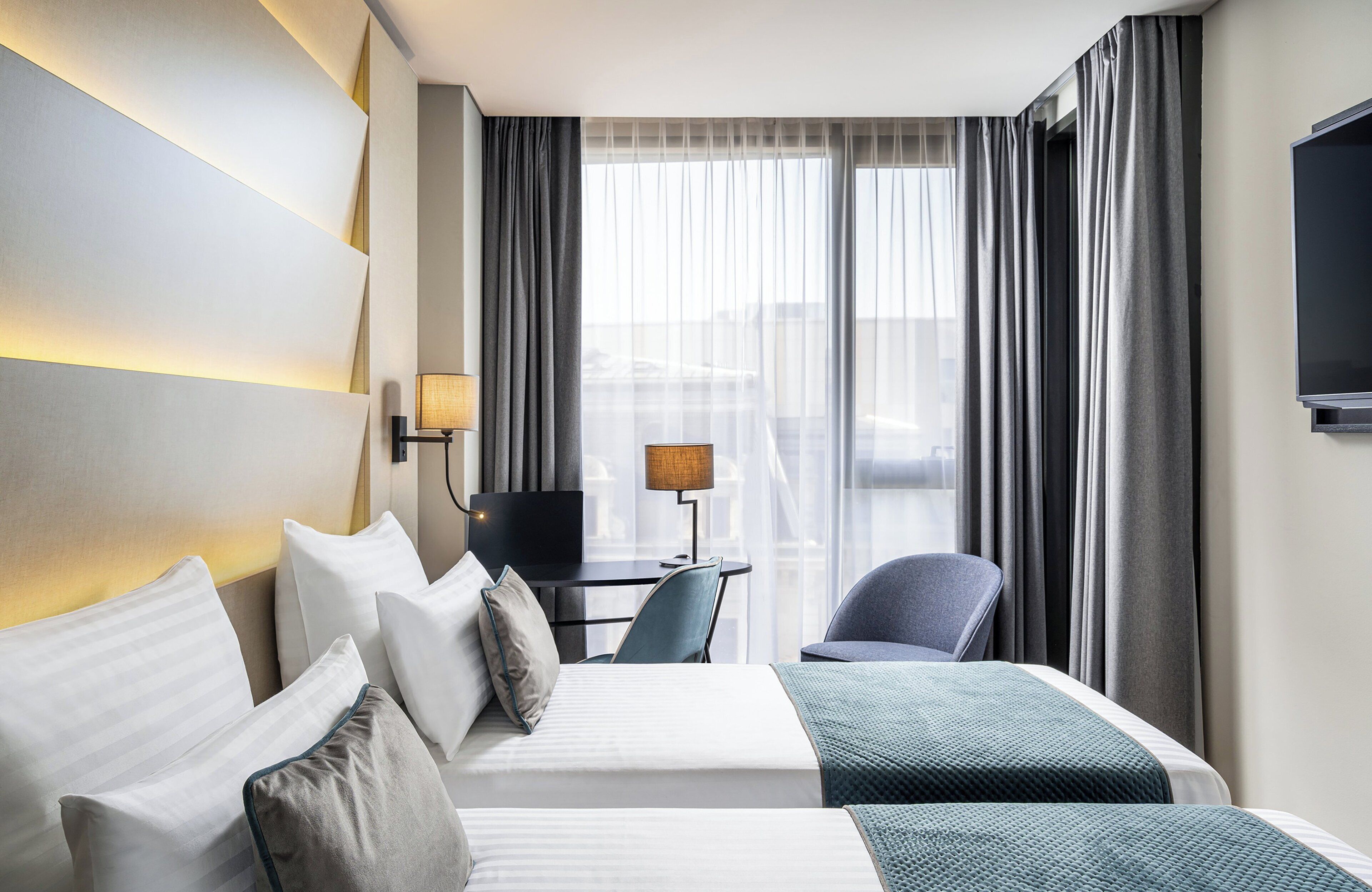 Una habitación de hotel con una cama, un escritorio con lámpara, una silla y un televisor.