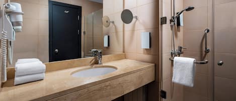 A bathroom with a sink, mirror, towel rack, and a shower area.