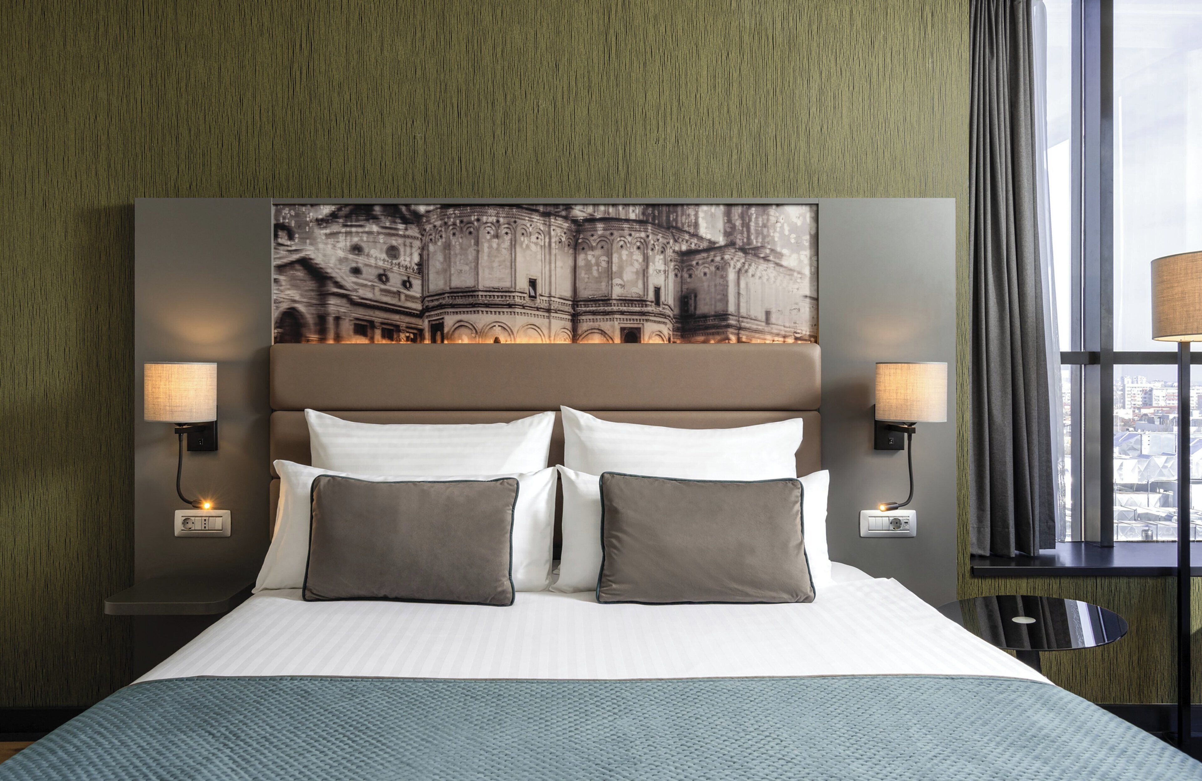 Een hotelkamer met een groot bed, twee bedlampen, uitzicht op de stad en een structuurwand.