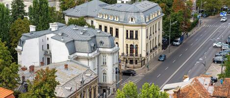 A historic building with classical architecture, a wide street, and parked cars.