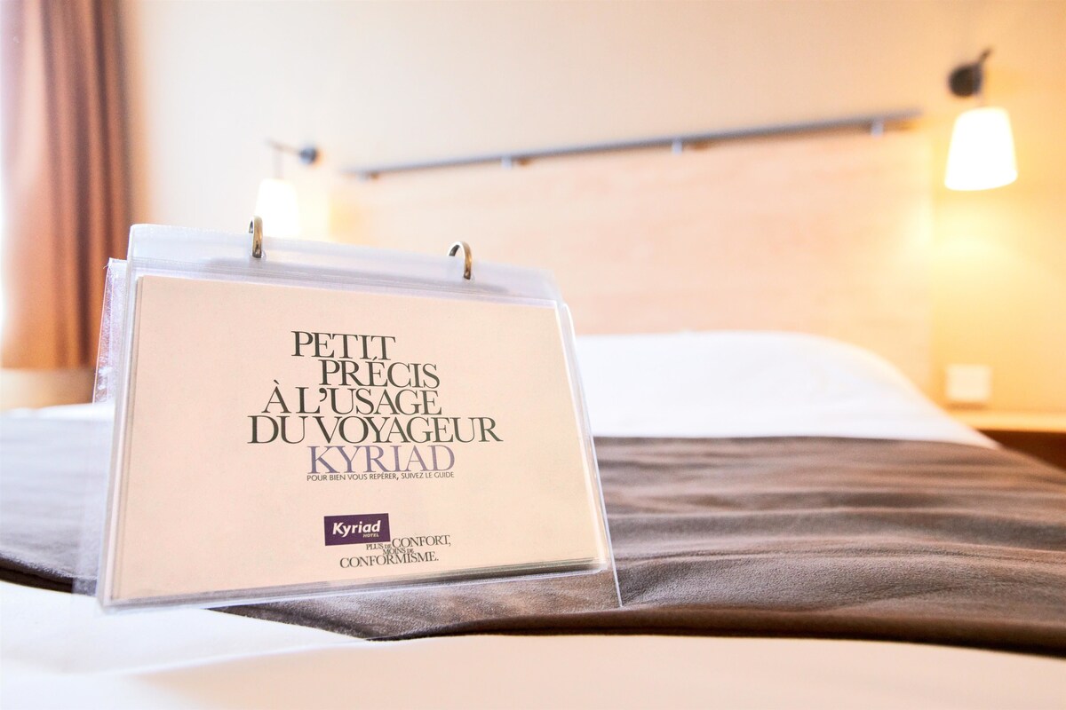 Una habitación de hotel con una cama, una mesita de noche y una lámpara fijada a la pared.