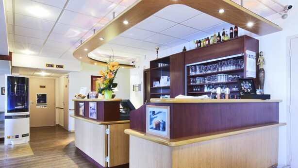 A bar area with wooden counters, shelves with bottles, and a decorative vase. - Hotel Kyriad Beauvais Sud (Beauvais)