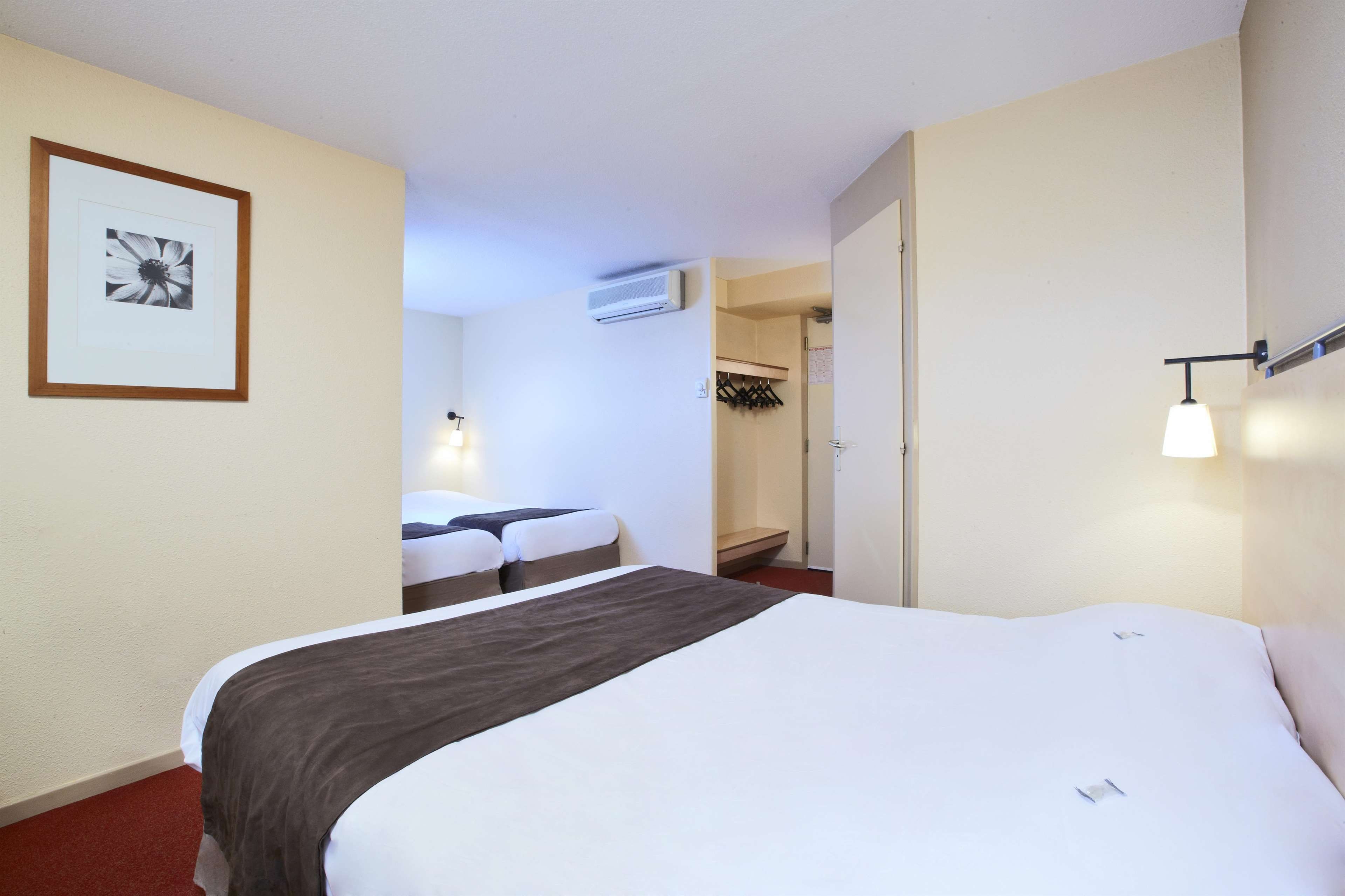 A hotel room with a bed, a bedside table, a framed picture on the wall, and a bathroom visible through an open door.