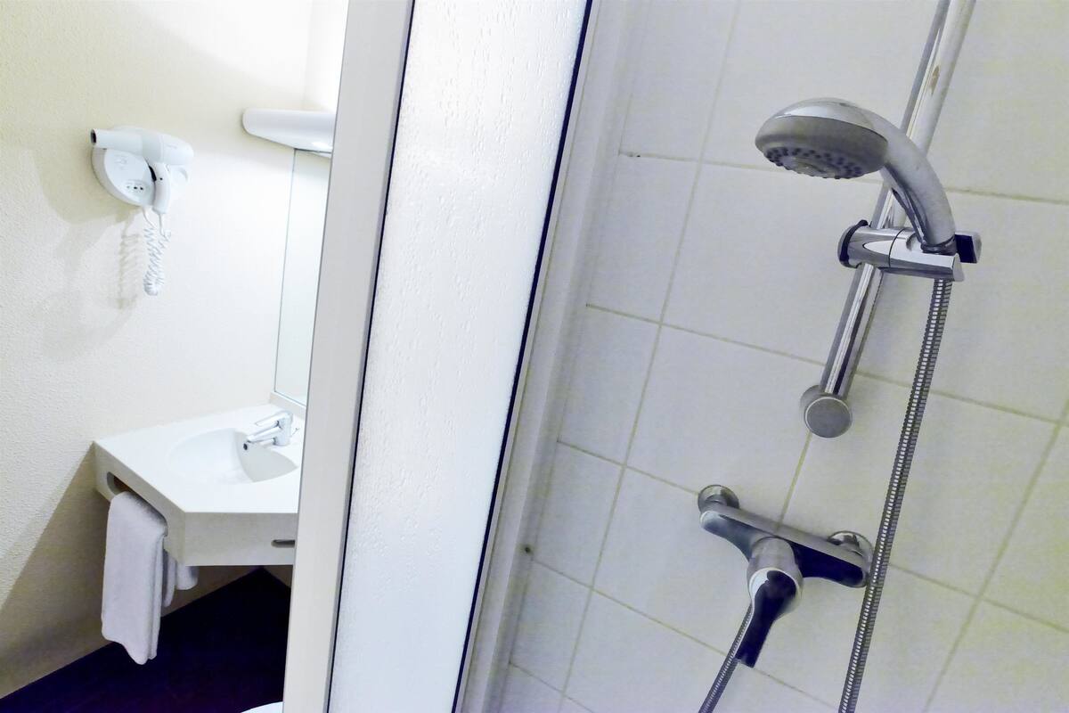 Casa de banho com uma pia branca, um porta-toalhas, um chuveiro com chuveiro manual e um telefone fixado na parede.