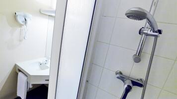 Un baño con un lavamanos blanco, un perchero para toallas, una ducha con cabezal de ducha de mano y un teléfono fijo en la pared.