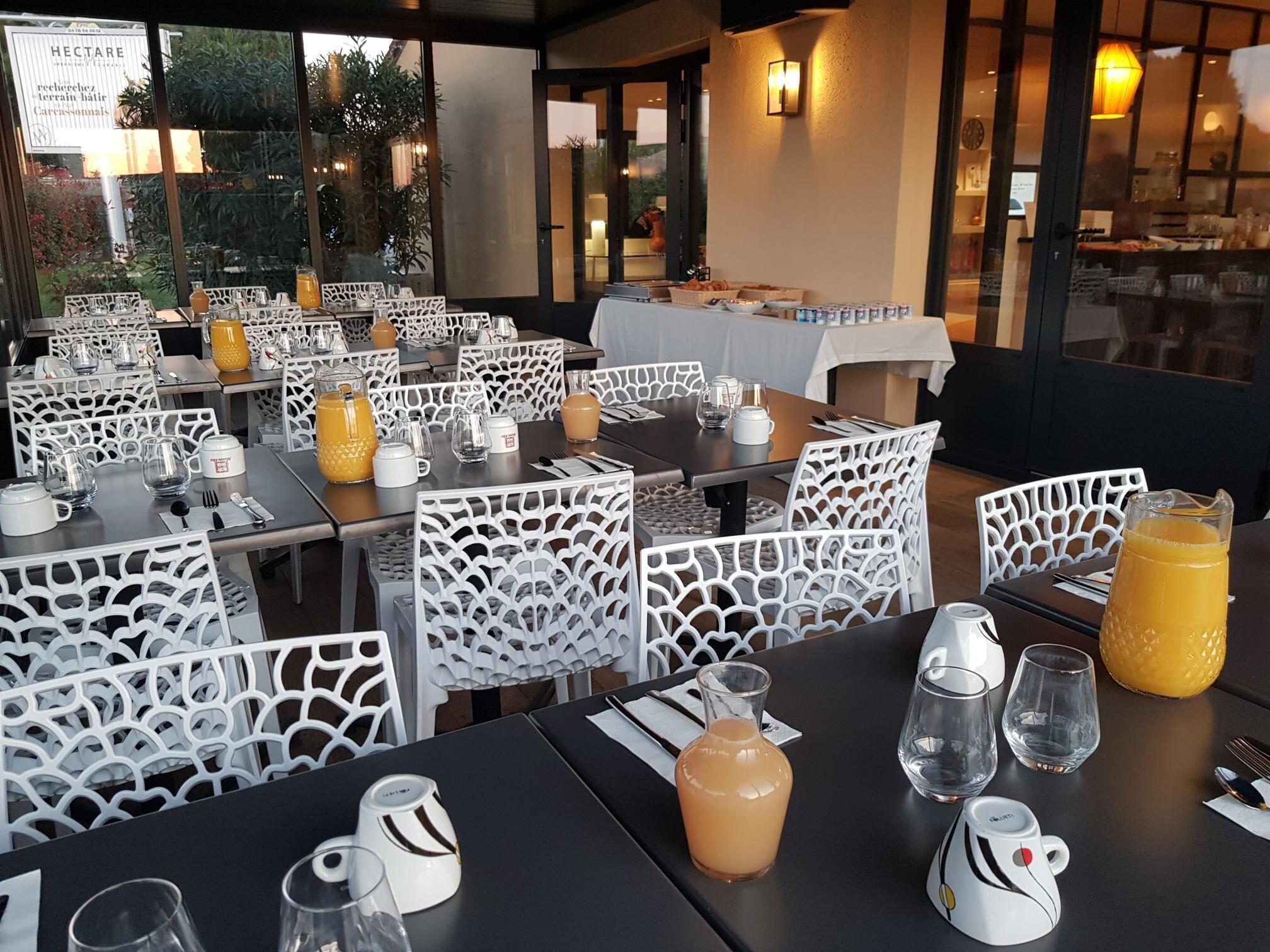 A restaurant with outdoor seating, white patterned chairs, and tables set with glasses, pitchers, and plates.