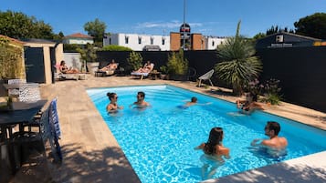Área de piscina com espreguiçadeiras e um restaurante ao fundo.