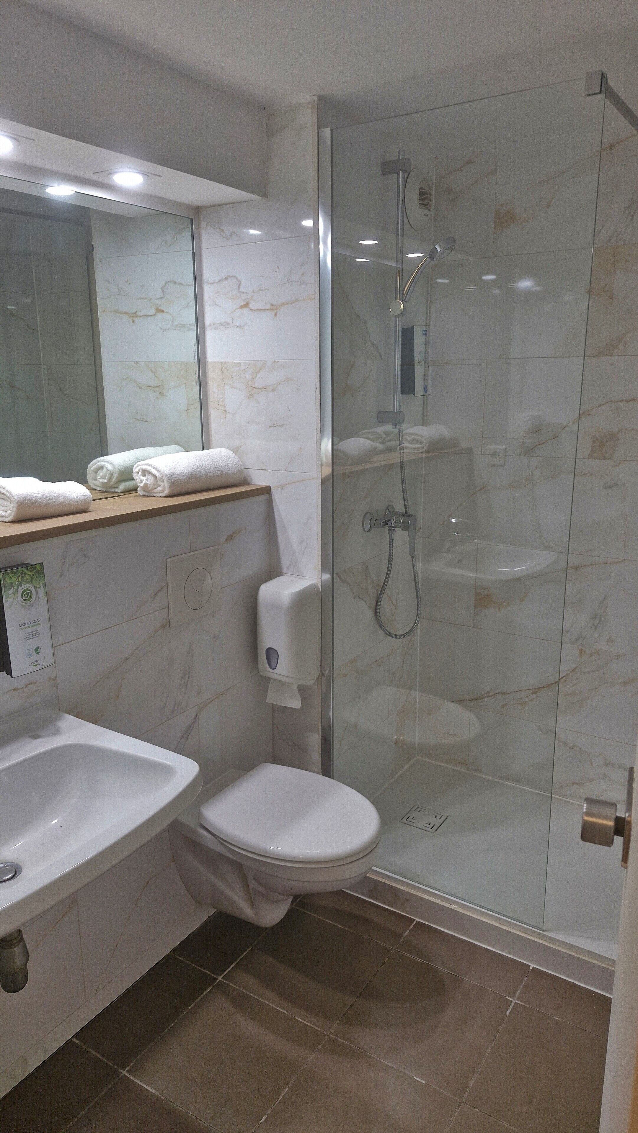 Un baño moderno con ducha envuelta en vidrio, un lavamanos blanco y un inodoro.