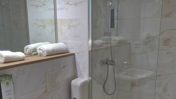 Un baño moderno con ducha envuelta en vidrio, un lavamanos blanco y un inodoro.