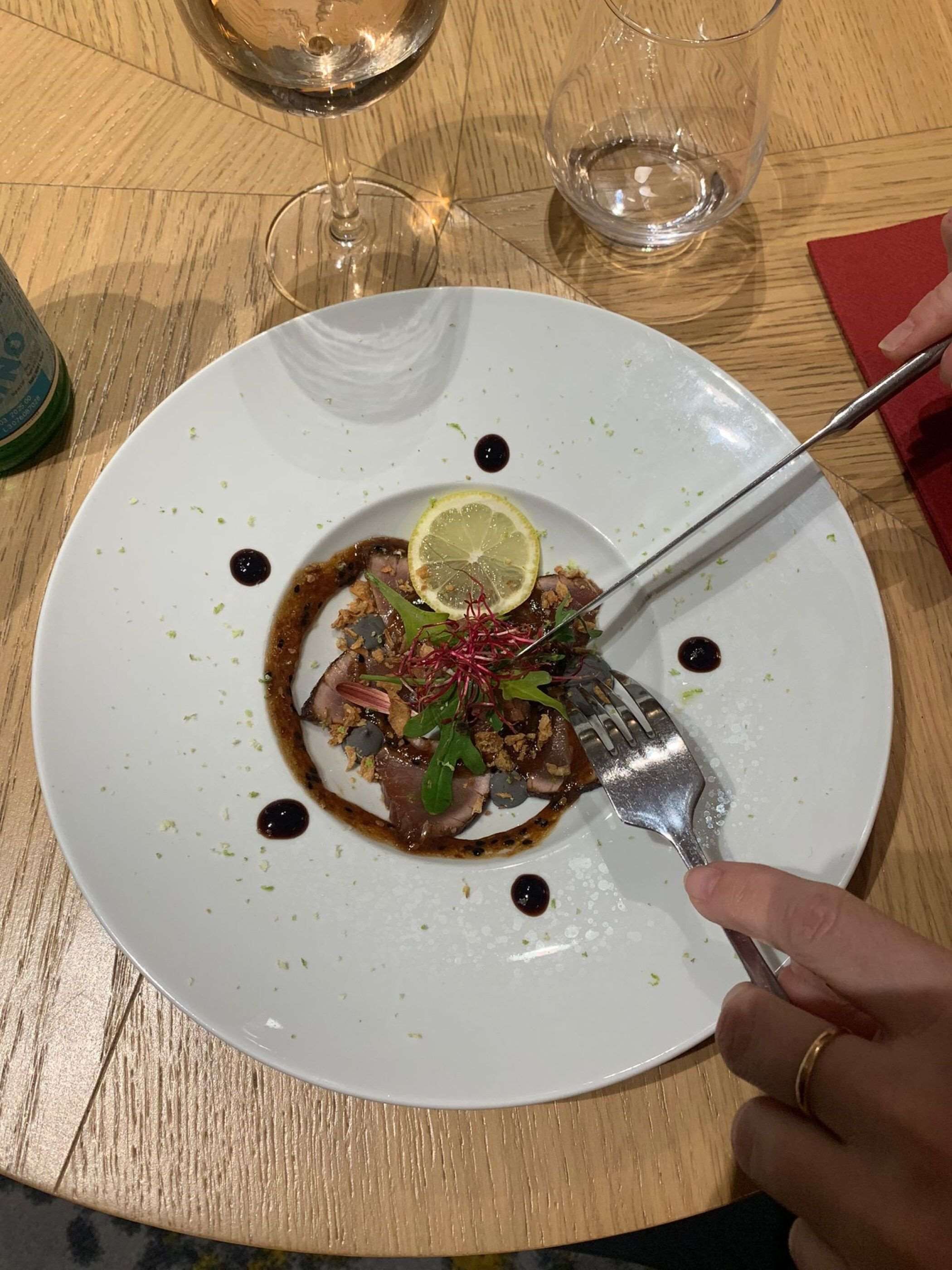 Une assiette blanche contenant un plat, une fourchette et un verre de vin, le tout posé sur une table en bois.