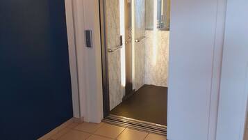 A hallway leading to an elevator with a marble finish and a light fixture above it.