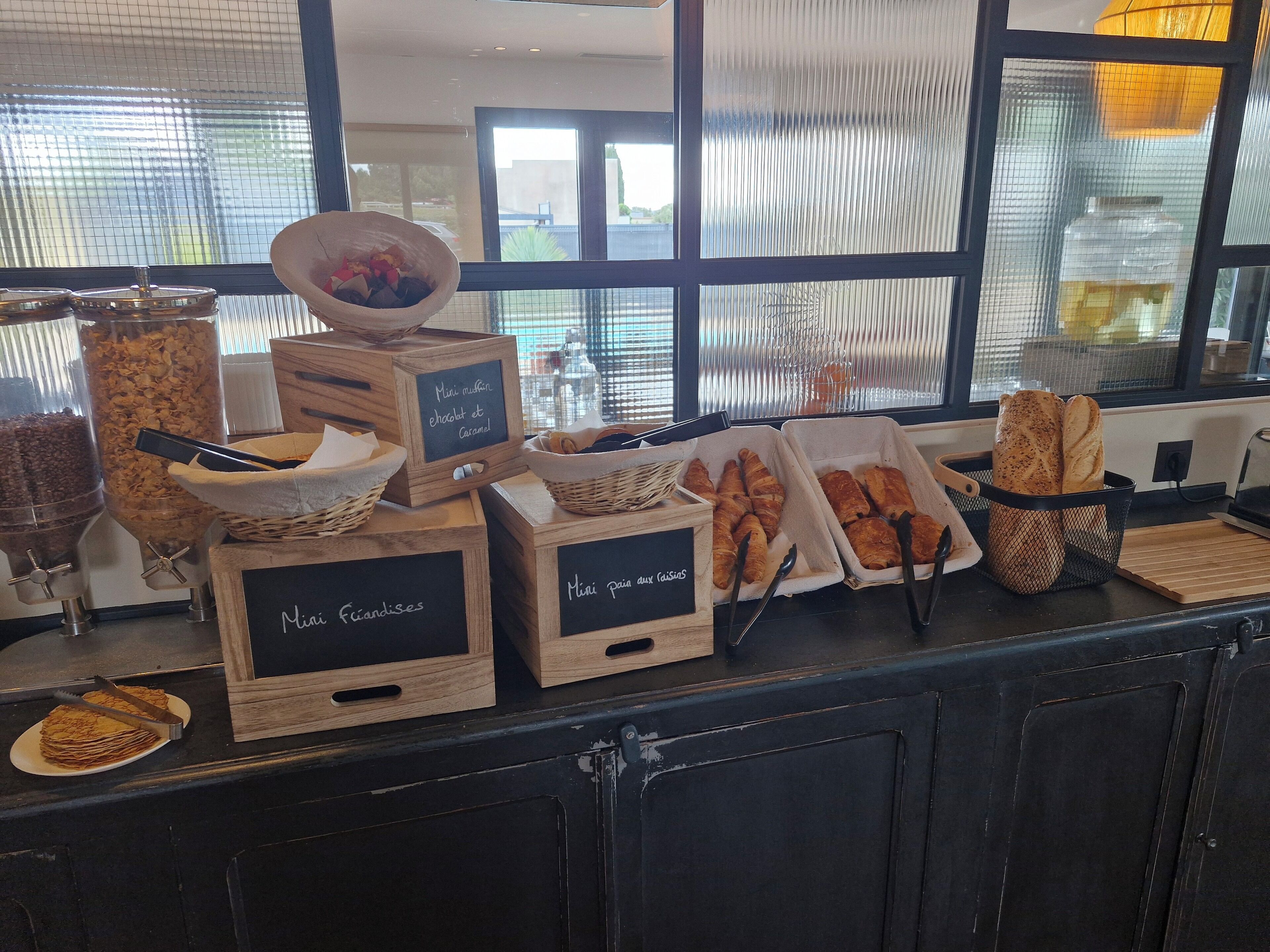 Um buffet de café da manhã com diversos alimentos e recipientes identificados em francês.