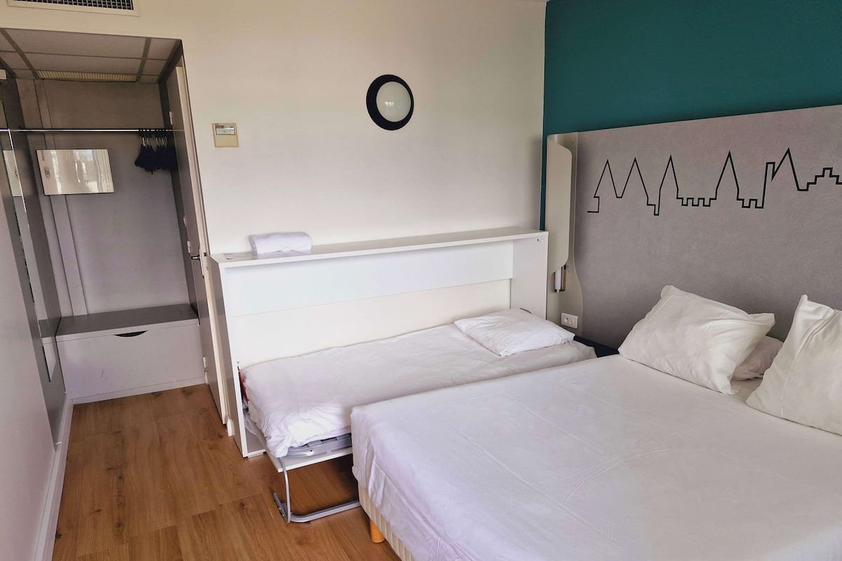 Una habitación de hotel con dos camas, un armario, un espejo y un reloj de pared.