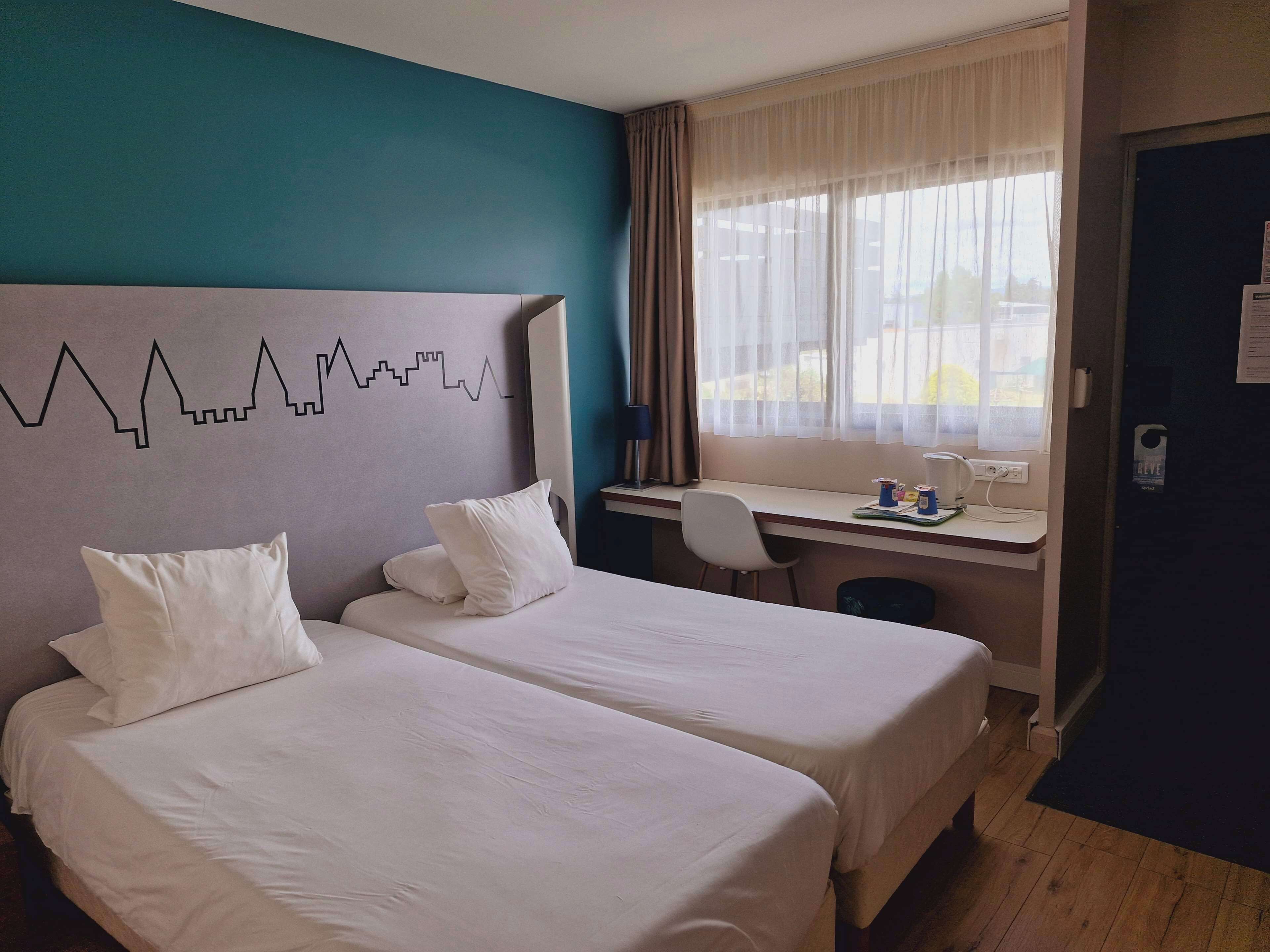 Et hotelværelse med to senge, et skrivebord og udsigt til det fri.