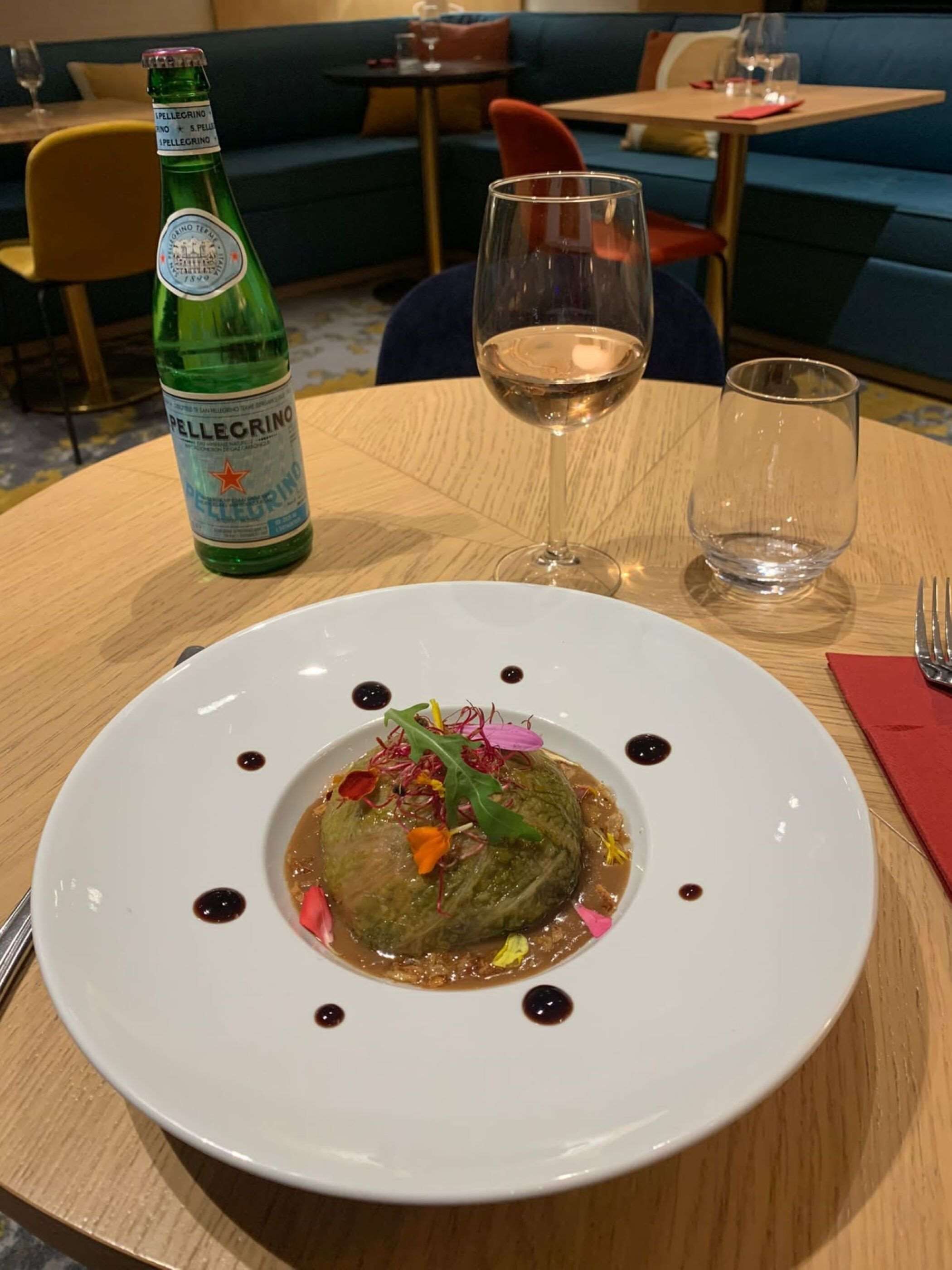A dining table with a bottle of Pellegrino water, a glass of white wine, and a plate of food.