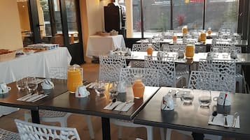 Restaurante com mesas preparadas para refeições, cadeiras brancas e vista para o exterior.