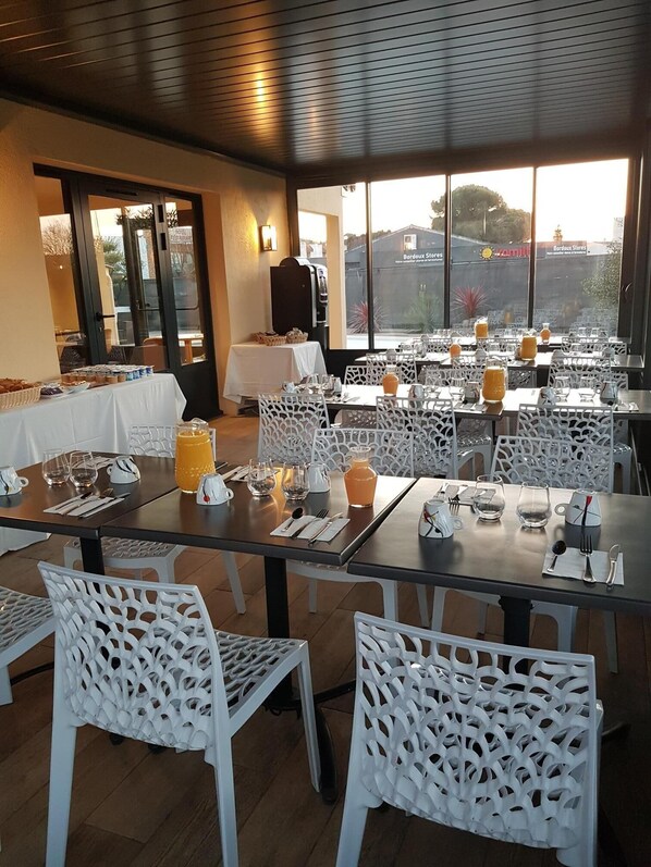 Un restaurante con mesas preparadas para comer, sillas blancas y vistas al exterior.