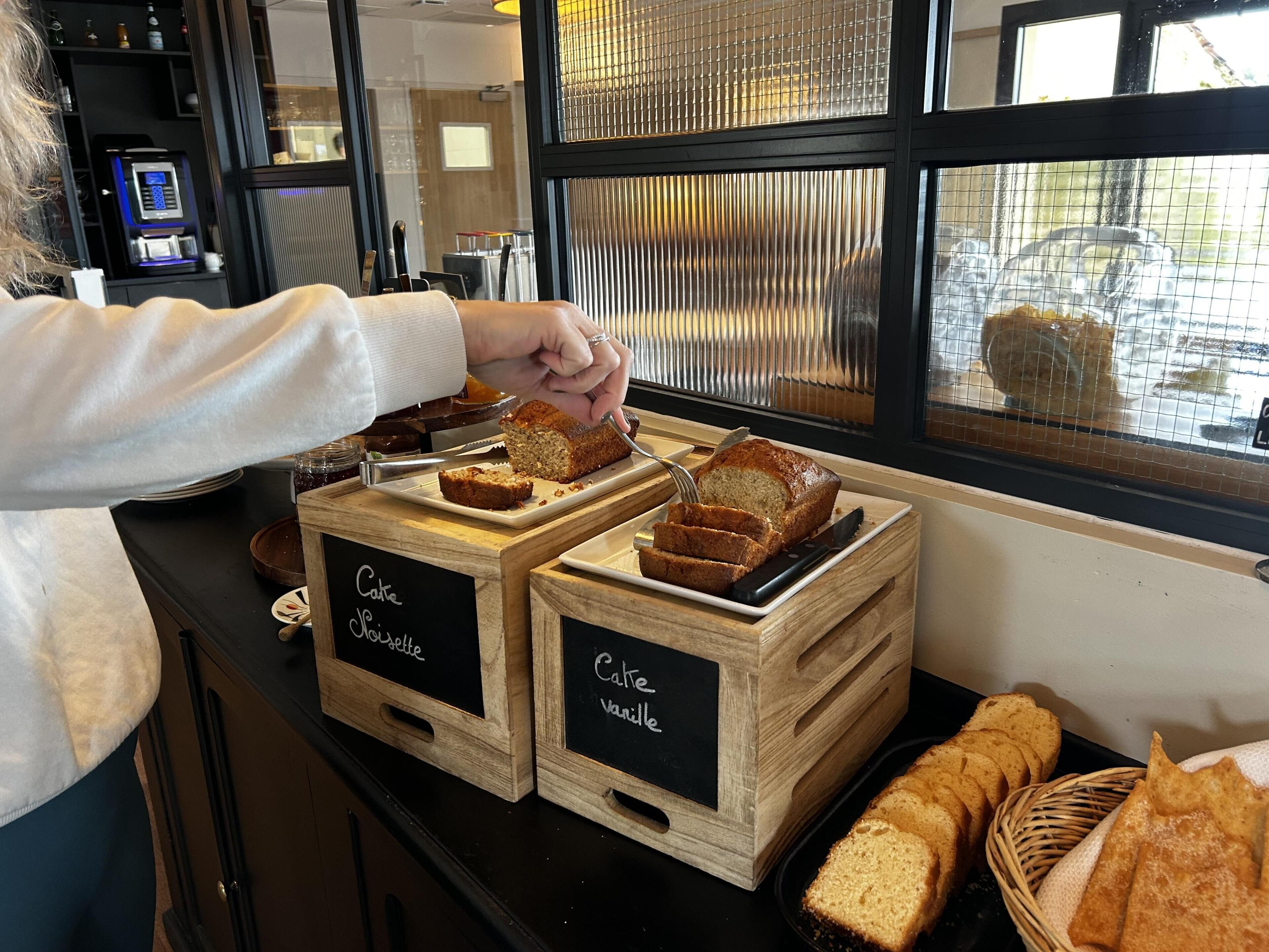 Mostrador de panadería con dos cajas de madera que dicen 'Café Moellette' y 'Café vanille', con rebanadas de pan y una hogaza.
