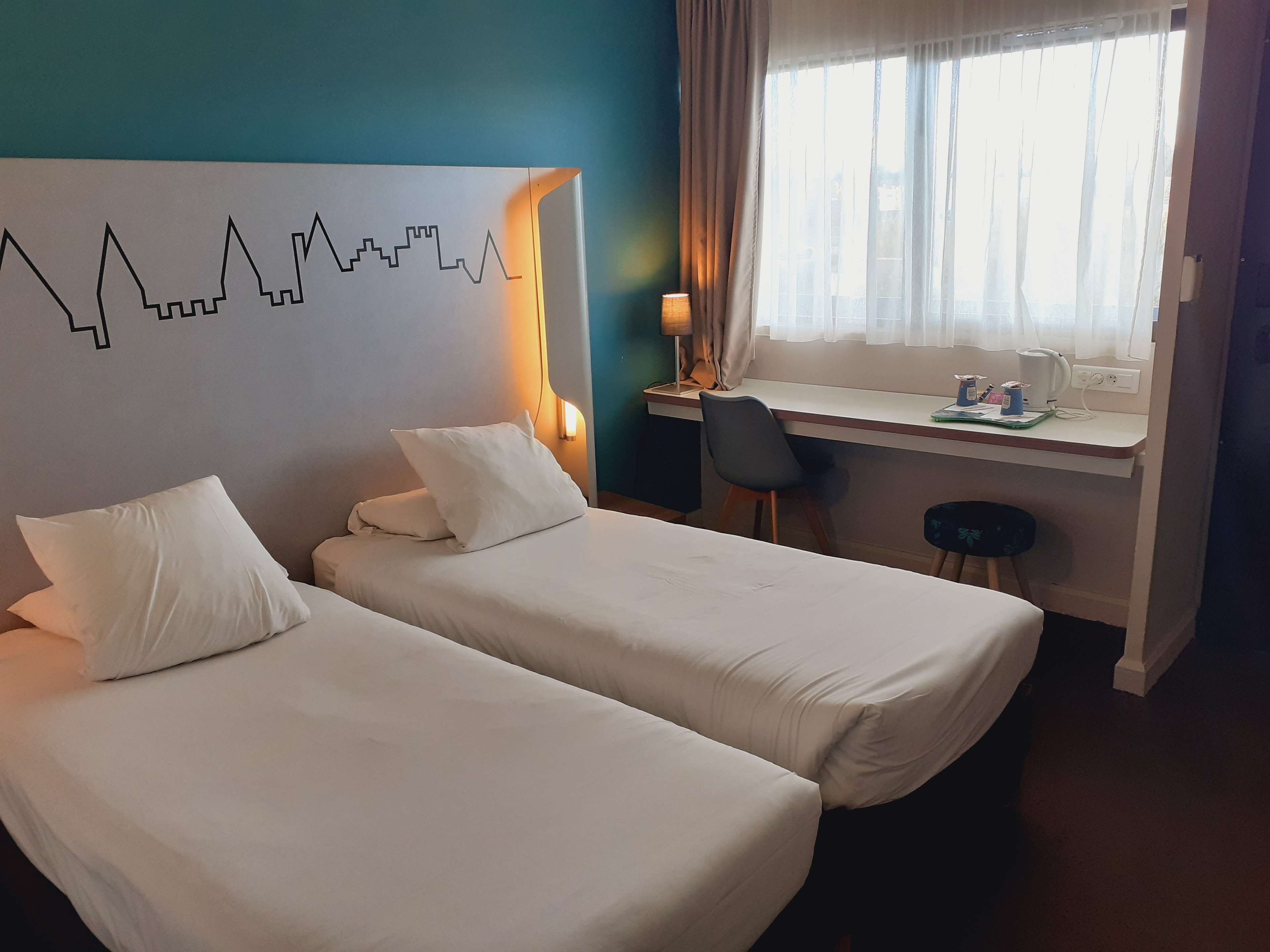 Ein Hotelzimmer mit zwei Betten, einem Schreibtisch, einem Stuhl und einem Fenster mit Vorhängen.