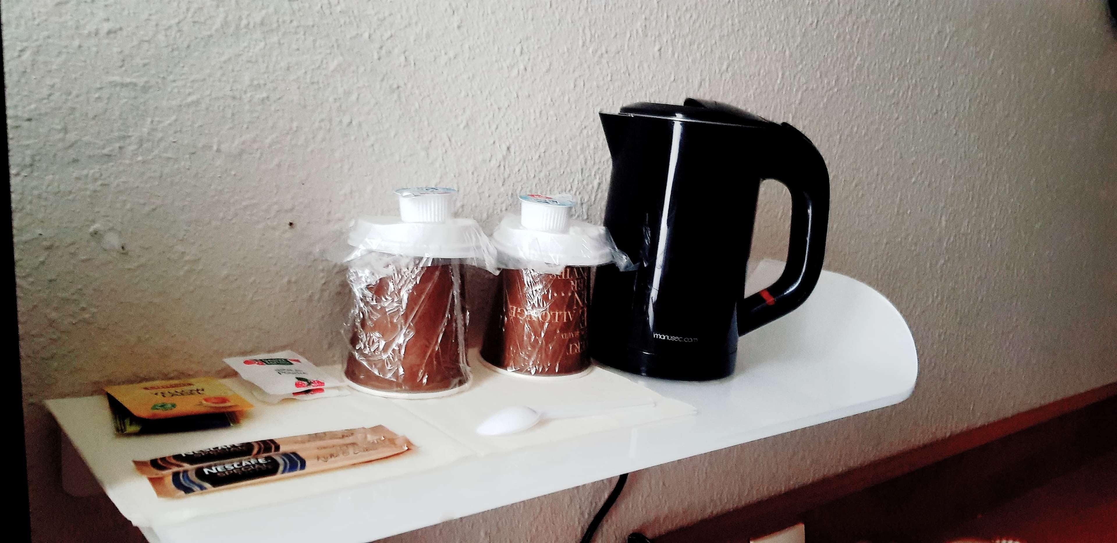 A white shelf with a black coffee maker, two glass bottles with white caps, a white mouse, and a packet of Nescafe coffee.