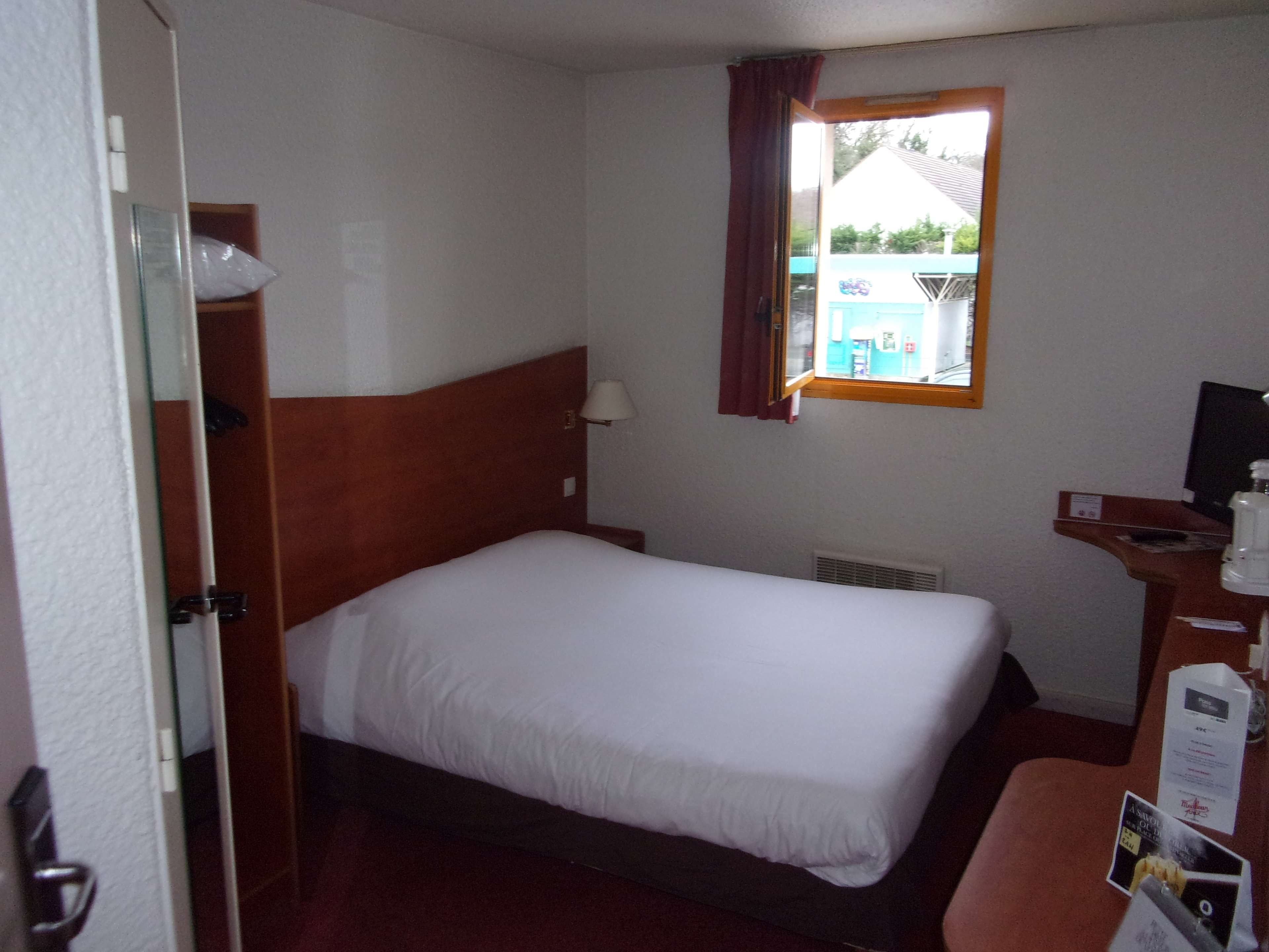 Habitación de hotel con una cama individual, un escritorio con computadora, una ventana con cortinas y vistas al exterior.