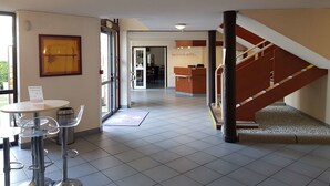 A hotel lobby with a reception desk, a staircase, and a seating area with bar stools. - Kyriad Chantilly (Gouvieux)