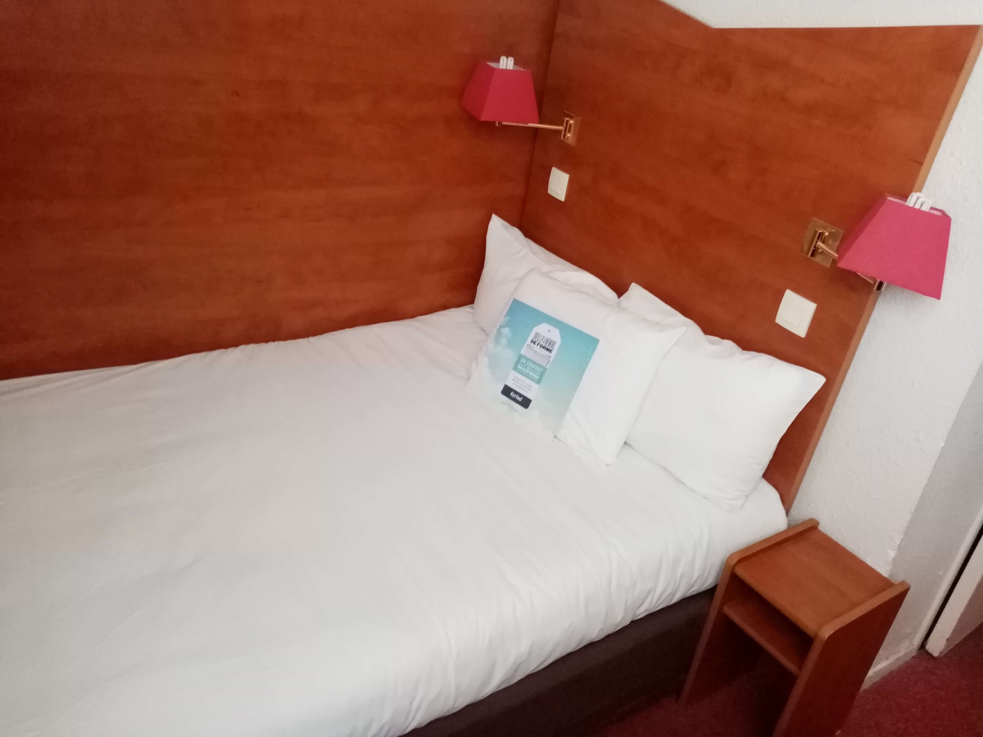 Un lit avec une literie blanche, un oreiller avec une étiquette et deux lampes de chevet.