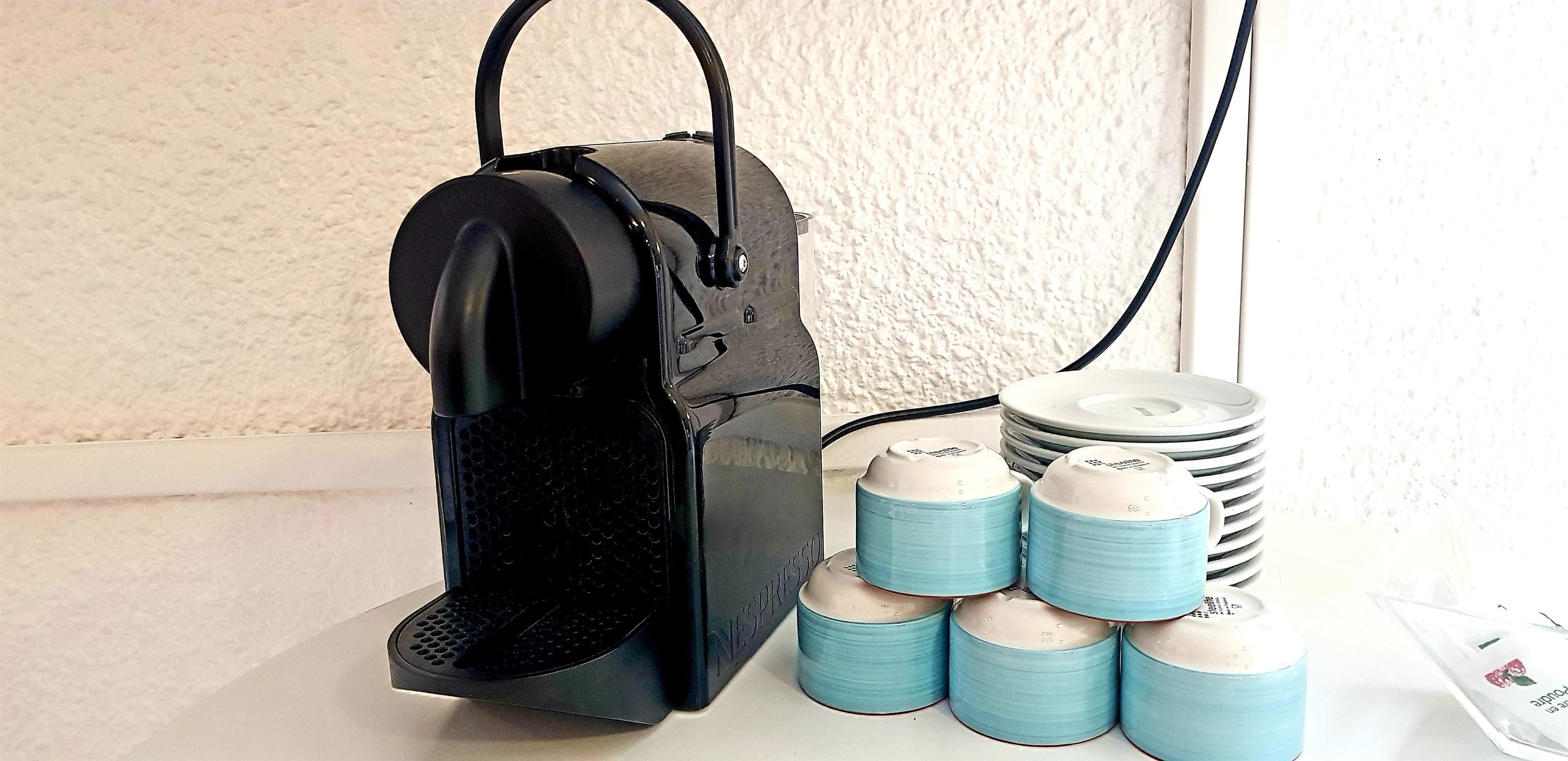 A coffee machine with a black handle and a control panel, next to a stack of blue and white cups and a coffee pod.