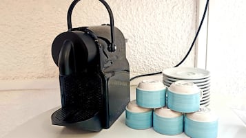 A coffee machine with a black handle and a control panel, next to a stack of blue and white cups and a coffee pod.