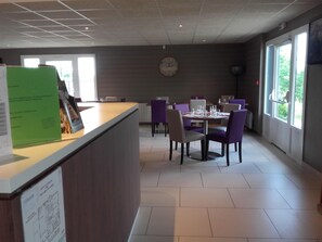 A modern dining area with a reception desk, purple chairs, and a clock on the wall. - Campanile Sable Sur Sarthe (Vion)