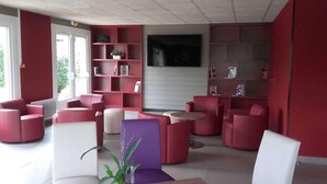 Un moderno salón con mobiliario rojo y blanco, un ventanal grande y una estantería.