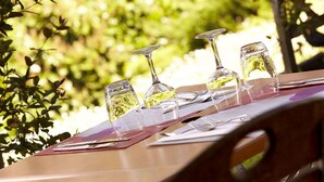 Una mesa con copas de vino y una carta, al aire libre con follaje de fondo.