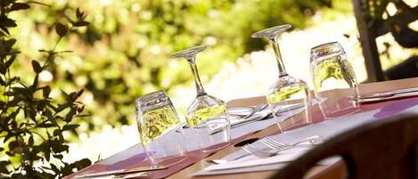 A table with wine glasses and a menu, set outdoors with greenery in the background.