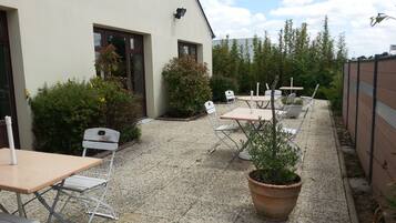 An outdoor patio area with tables and chairs, surrounded by greenery and a building.